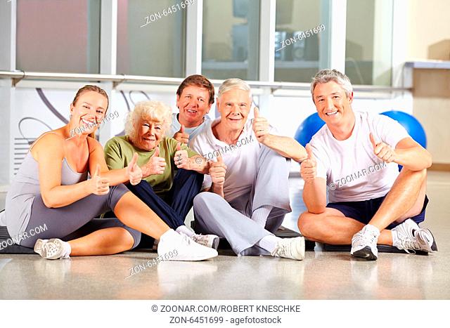 Eine Gruppe glücklicher Senioren hält die Daumen hoch im Fitnesscenter