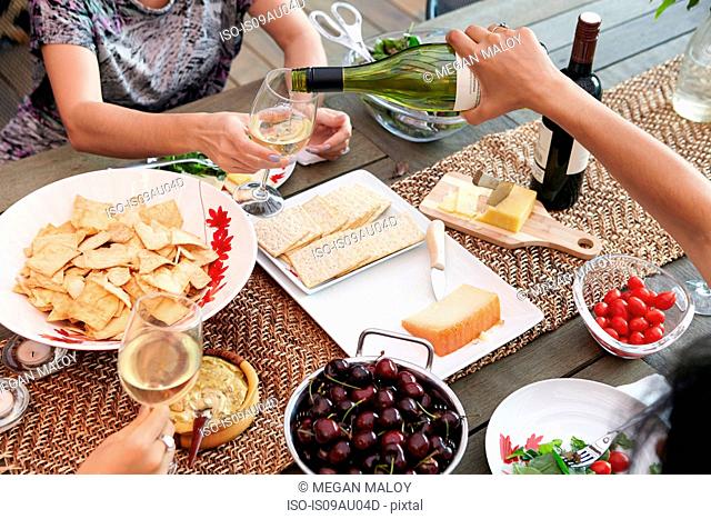 Cropped overhead view of female friends pouring wine at lunch table
