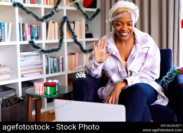 Happy african american woman wearing santa claus hat, using laptop for video call