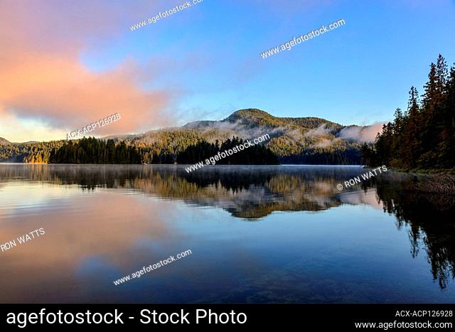 The morning sun illuminates the far shore of Main Lake, in Main Lake Provincial Park on Quadra Island, British Columbia, Canada