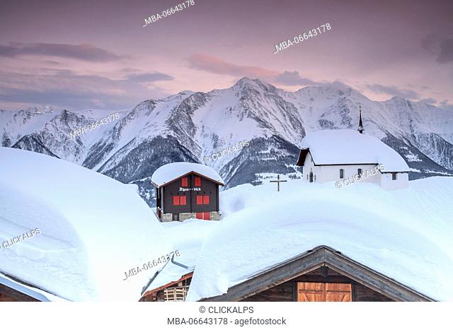 Pink sky at sunset frames the snowy mountain huts and church Bettmeralp district of Raron canton of Valais Switzerland Europe