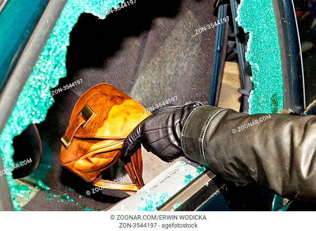 Ein Dieb entwendet eine Handtasche aus einem Auto durch eine zerbrochene Seitenscheibe