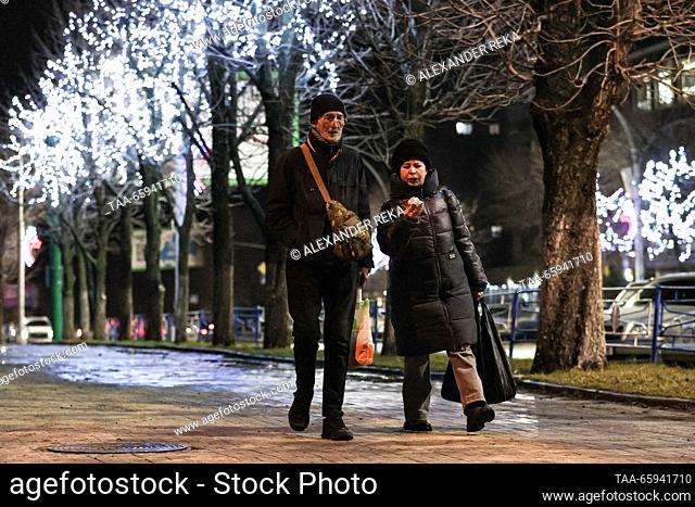 RUSSIA, LUGANSK - 20 de diciembre de 2023: Un par de paseos mientras las luces de cuerda cuelgan de los árboles en la plaza del jardín de la Guardia joven