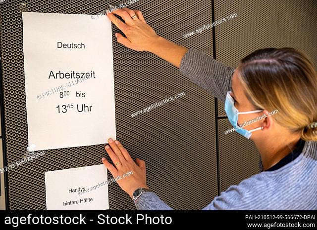 12 May 2021, Bavaria, Munich: A teacher at the Wilhelmsgymnasium, hangs a note on the wall in the auditorium with the working time for the German Abitur