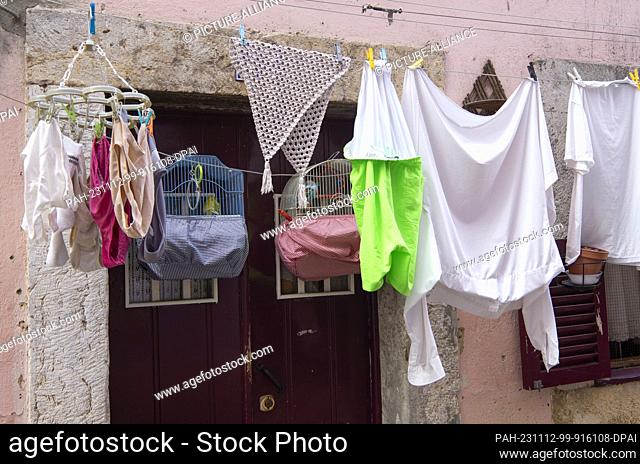 PRODUCTION - 27 October 2023, Portugal, Lissabon: Birdcages with birds and laundry hang outside a front door in an alleyway in Lisbon's Alfama district