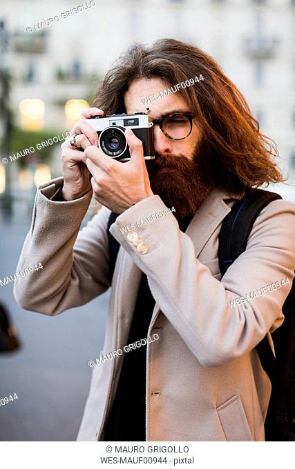 Stylish young man outdoors taking pictures with old-fashioned camera