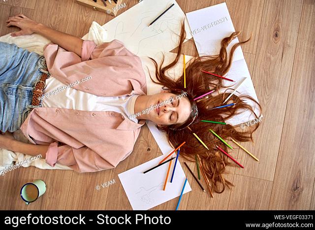 Smiling female artist lying down with colored pencil in hair while eyes closed at home