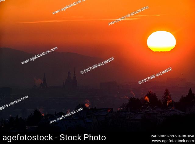 07 February 2023, Saxony, Dresden: The sun rises in the morning over the Elbe valley near the old town with the Hofkirche (l-r)
