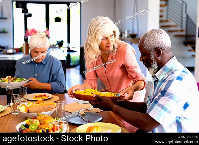 Multiracial senior woman serving food to male friend at dining table in nursing home