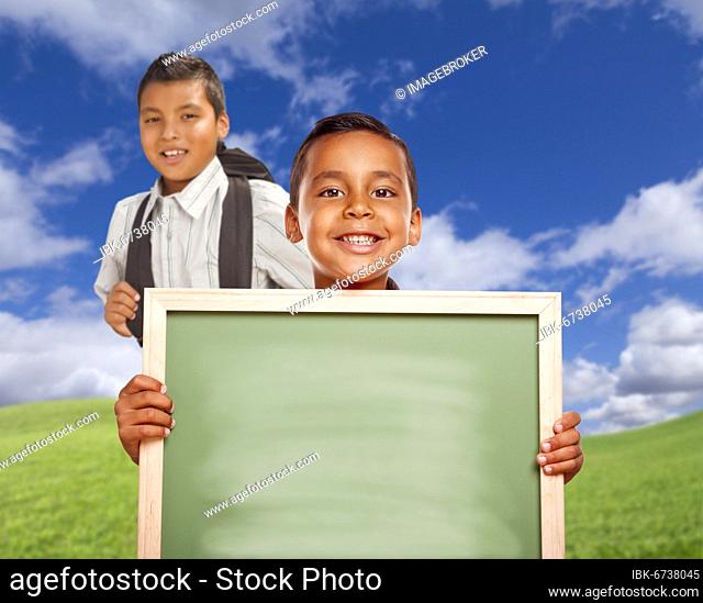 Smiling happy hispanic boys in grass field holding blank chalk board