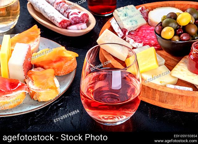 Rose wine with charcuterie, cheese, and salmon sandwiches. Spanish tapas. Jamon, fuet, goat and blue cheese and olives on a black background