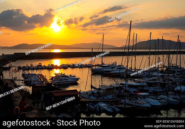 Alghero, Sardinia / Italy - 2018/08/10: Summer sunset skyline over the Alghero Marina yacht port at the Gulf of Alghero at Mediterranean Sea