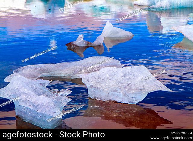 Cold July day. Bizarre icebergs and floating ice floes reflected in the smooth cold water of the lagoon. The lagoon Jokulsaurloun. Iceland