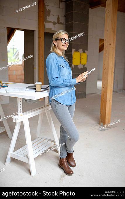 Smiling female building contractor looking away while holding at construction site