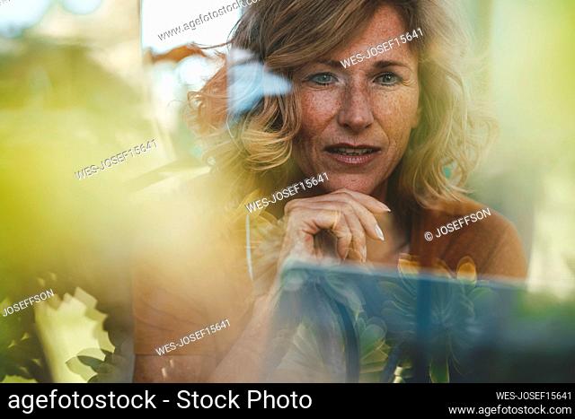 Smiling mature woman with tablet PC seen through glass window