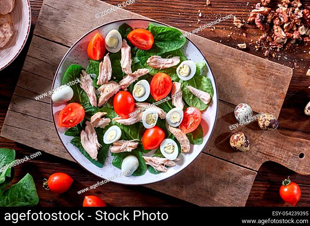 A plate of salad from boiled meat, quail eggs, spinach and tomatoes on a wooden board on the kitchen table. Dietary snack Flat lay