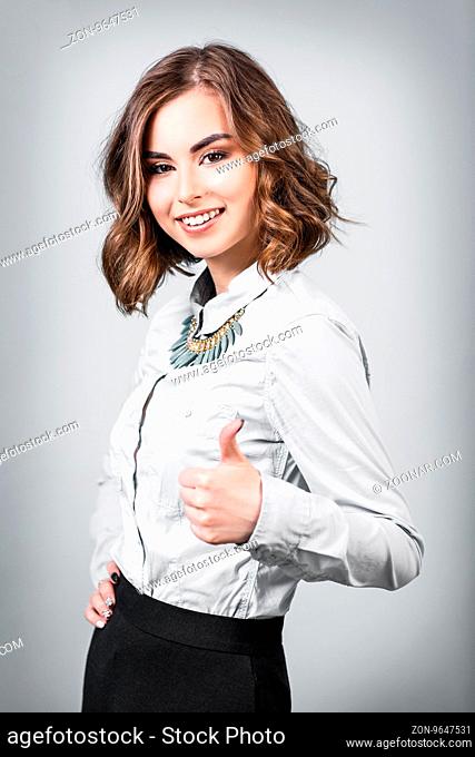 Gorgeous young woman showing thumbs up on the gray background