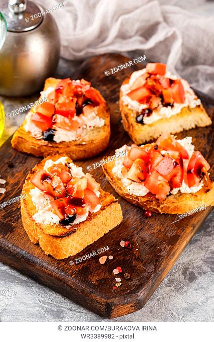 Bruschetta with tomatoes, mascarpone cheese and balsamic sauce on wooden cutting board on light background