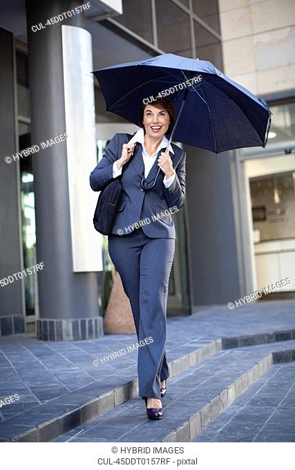 Businesswoman carrying umbrella outdoors