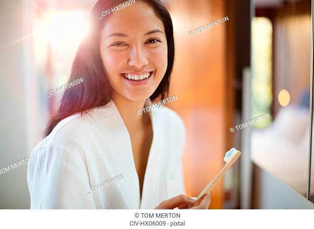 Portrait happy young woman brushing teeth in bathroom