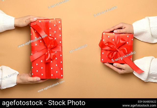 Female hands holding a gift box with a red ribbon on a brown background. View from above