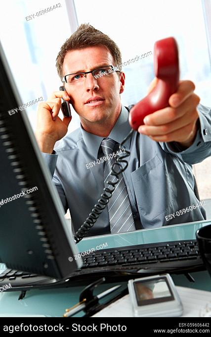 Businessman with glasses busy talking on mobile phone handing over landline call to answer in office