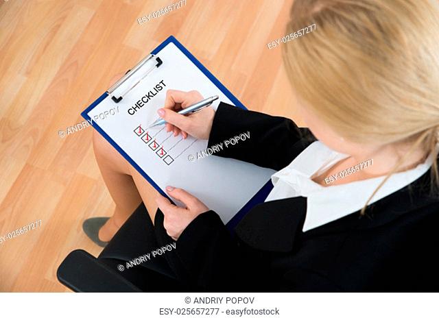Businesswoman Marking Checklist With Pen On Clipboard At Workplace