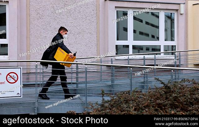 17 March 2021, Saxony, Erfurt: A police officer comes out of an apartment building with a box during a raid. Officers searched numerous apartments in several...