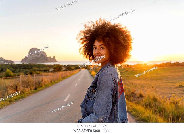 Young woman standing on street and looking at camera at sunset, Ibiza