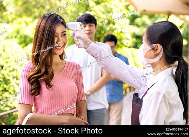 Asian waitress with face mask take temperature customer before getting in restaurant with social distance queue in line. Restaurant New normal restaurant...