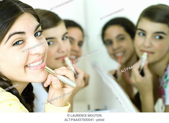 Three young female friends putting on make-up, smiling at camera