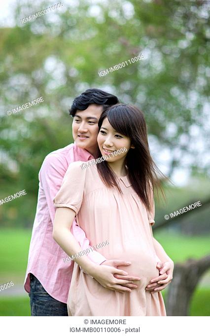 Young man embracing pregnant woman and looking away with smile