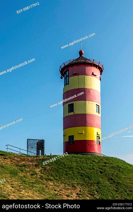 Pilsum Lighthouse standing on the dike. View from below against clear blue sky. The Pilsum Lighthouse was built in 1891 and is located near the East Frisian...