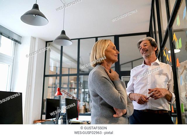 Businessman and businesswoman working on sticky notes at glass pane in office