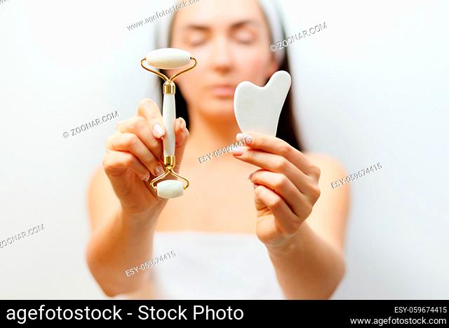 Natural Jade Face Lifting Gouache Scraper Massager. Beautiful Woman Using face roller and Gua Sha scraper over skin. beauty face skin care at home