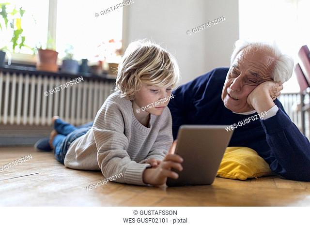 Grandfather and grandson lying on the floor at home using a tablet