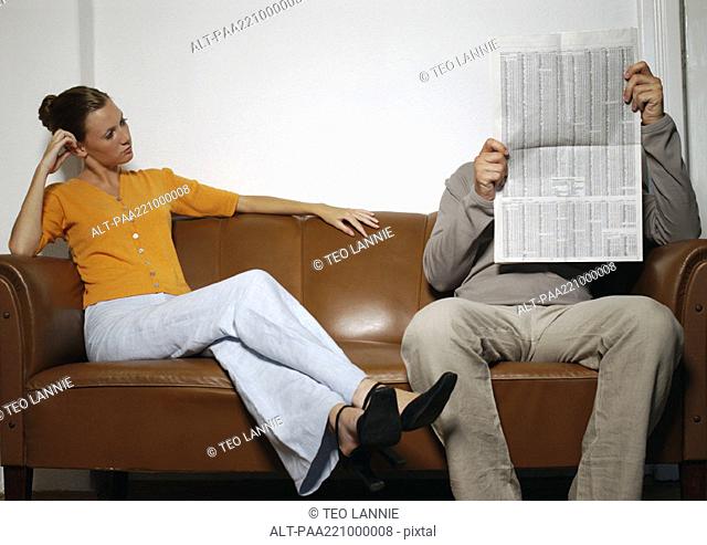 Man and woman sitting on sofa, man reading newspaper