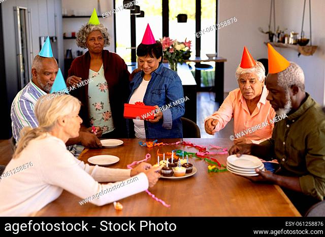 Multiracial senior friends wearing party hats doing preparation while woman holding birthday gift