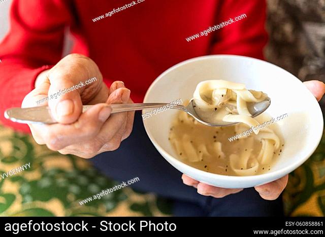 above view of bowl with chicken noodle soup in hand of old woman (focus on noodles in tablespoon)