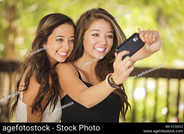 Two attractive mixed-race girlfriends taking self portrait with their phone camera outdoors