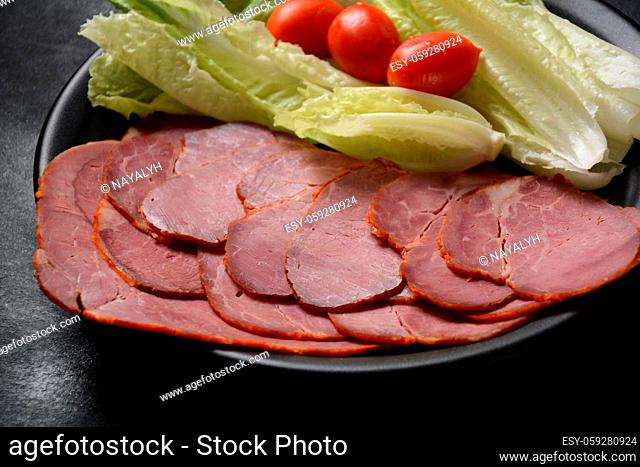 Smoked sliced beef with cherry tomatoes and lettuce on black plate