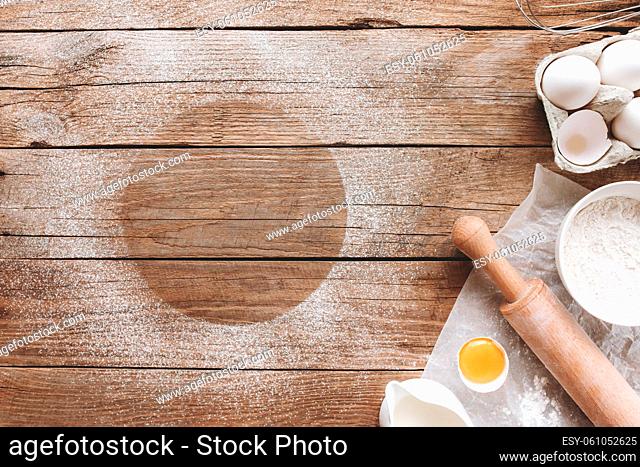 Baking ingredients, kitchen utensils on old wooden background. Cooking dough, preparing egg yolk, flour, rolling pin, milk, parchment paper, whisk, salt, sodium