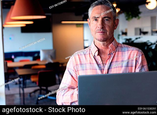 Portrait of serious caucasian mature businessman with laptop in creative office
