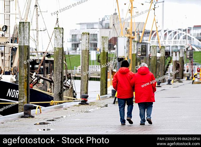 25 March 2023, Lower Saxony, Bensersiel: Tourists walk along a quay wall in the harbor in changeable weather. With the start of the vacations in Lower Saxony...