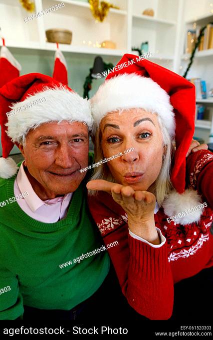 Portrait of senior couple in santa hat sitting on couch and blowing flying kisses at camera at home