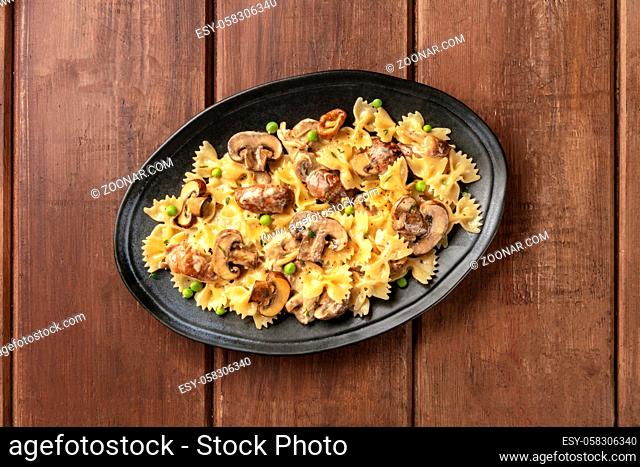 Mushroom and cheese pasta. Farfalle with cremini and green peas, shot from above on a dark rustic wooden background