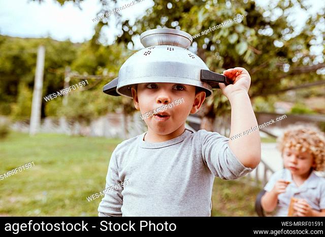 Playful boy wearing colander while playing on meadow