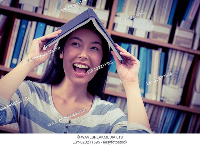 Funny student holding book on her head at the university
