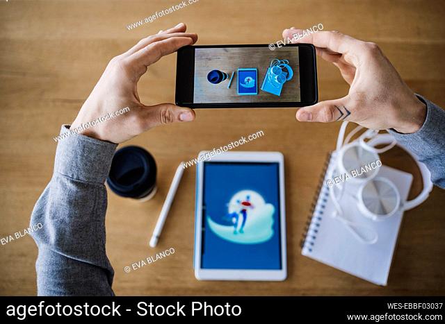 Creative male businessperson photographing graphics tablet and coffee cup on desk
