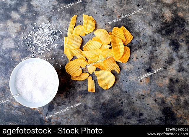 Directly above shot of rock salt in bowl with potato chips on table